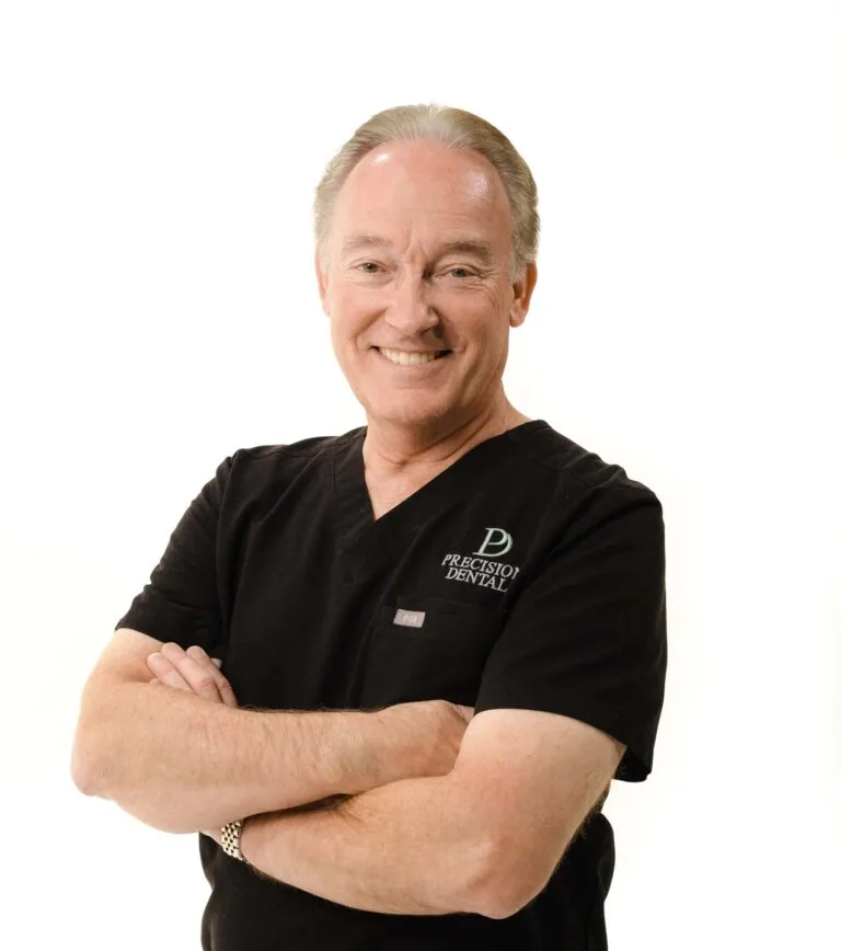 A man standing and wearing black scrubs while crossing his arms in a plain white background.