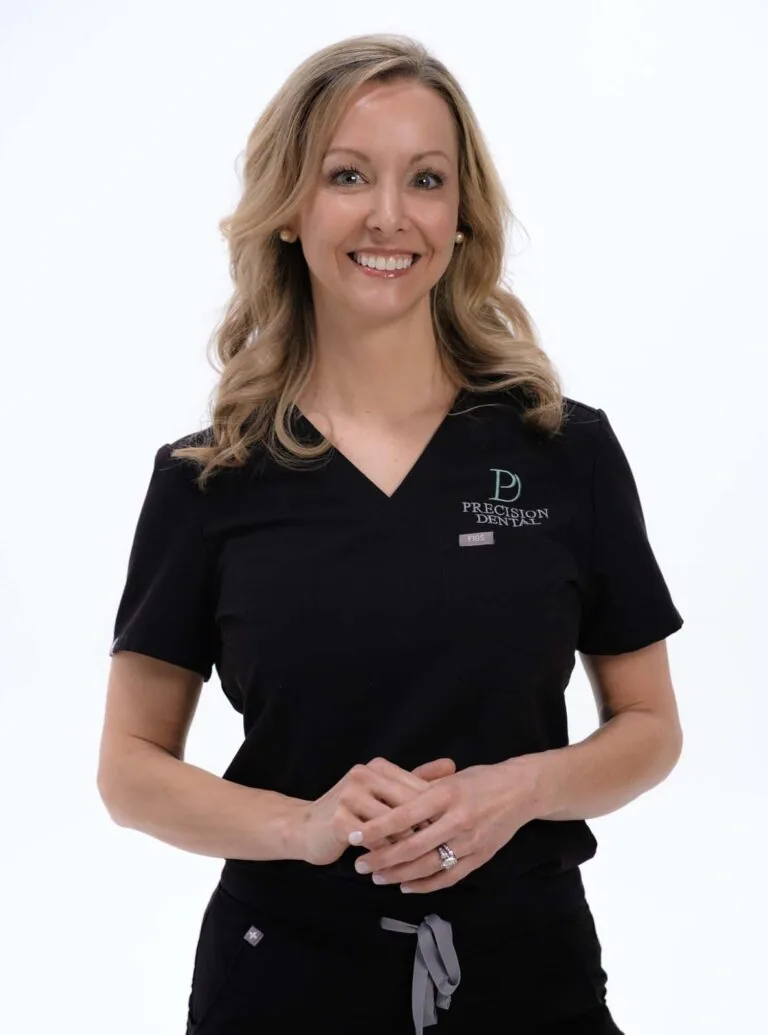 A photo of Dr. Greer standing and wearing a black scrubs with a logo of 'PRECISION DENTAL' on the right side of her chest, the background is plain white.