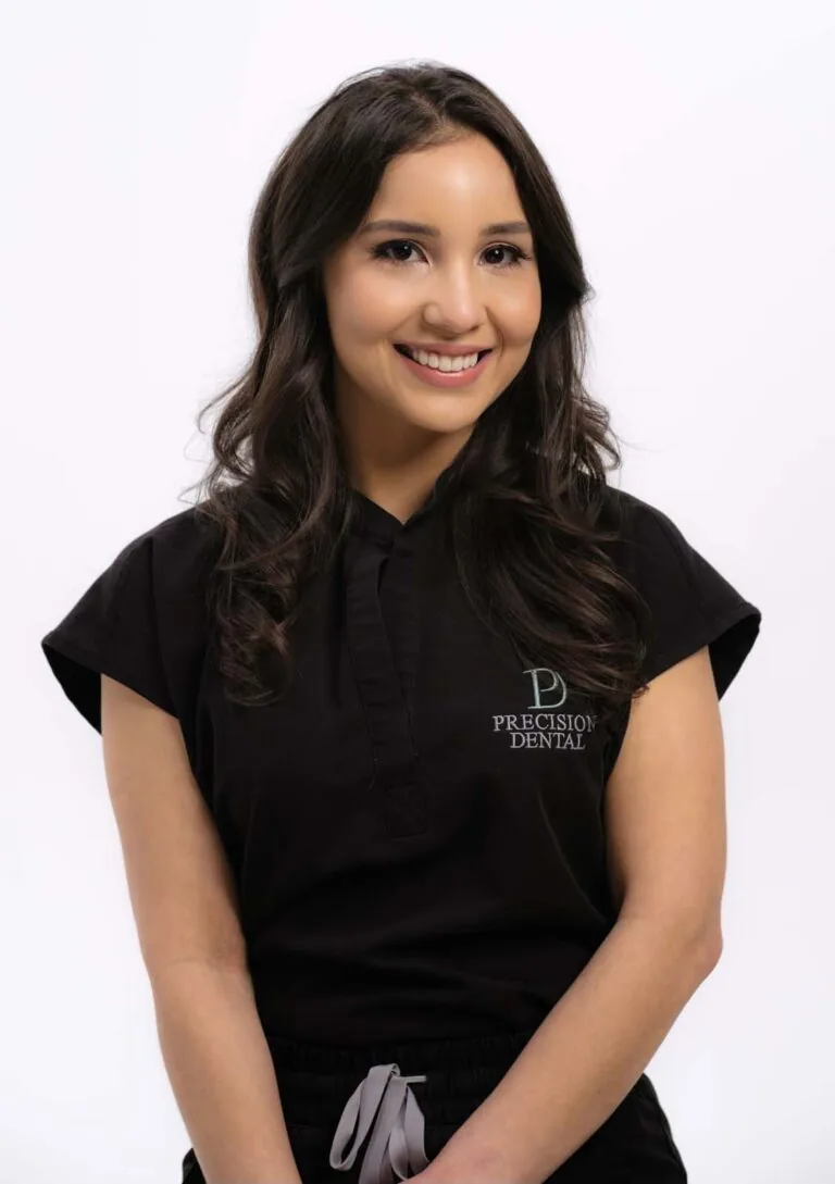 A photo Dr. Robertha Jones smiling and wearing a black scrubs with a logo of 'PRECISION DENTAL' on her right chest. The background is a plain white.