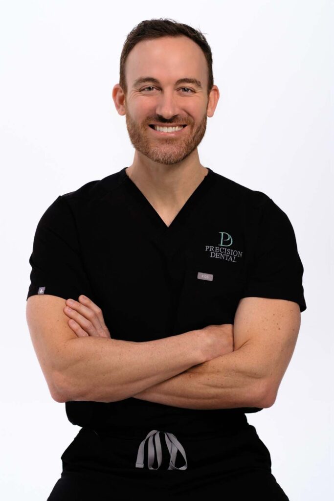 A photo of Dr. Bryan Packard crossing his arms and wearing a black scrubs with the logo of 'PRECISION DENTAL' in a plain white background.